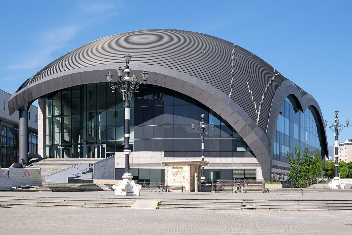The Macedonian Philharmonic in Skopje: a ribbed steel shell curving over a glass entrance, seen from the square in front