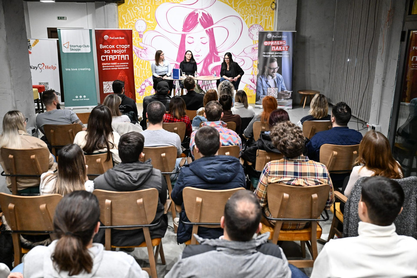 A full room at Srekja during a Startup Club Skopje panel, with the mural behind the speakers
